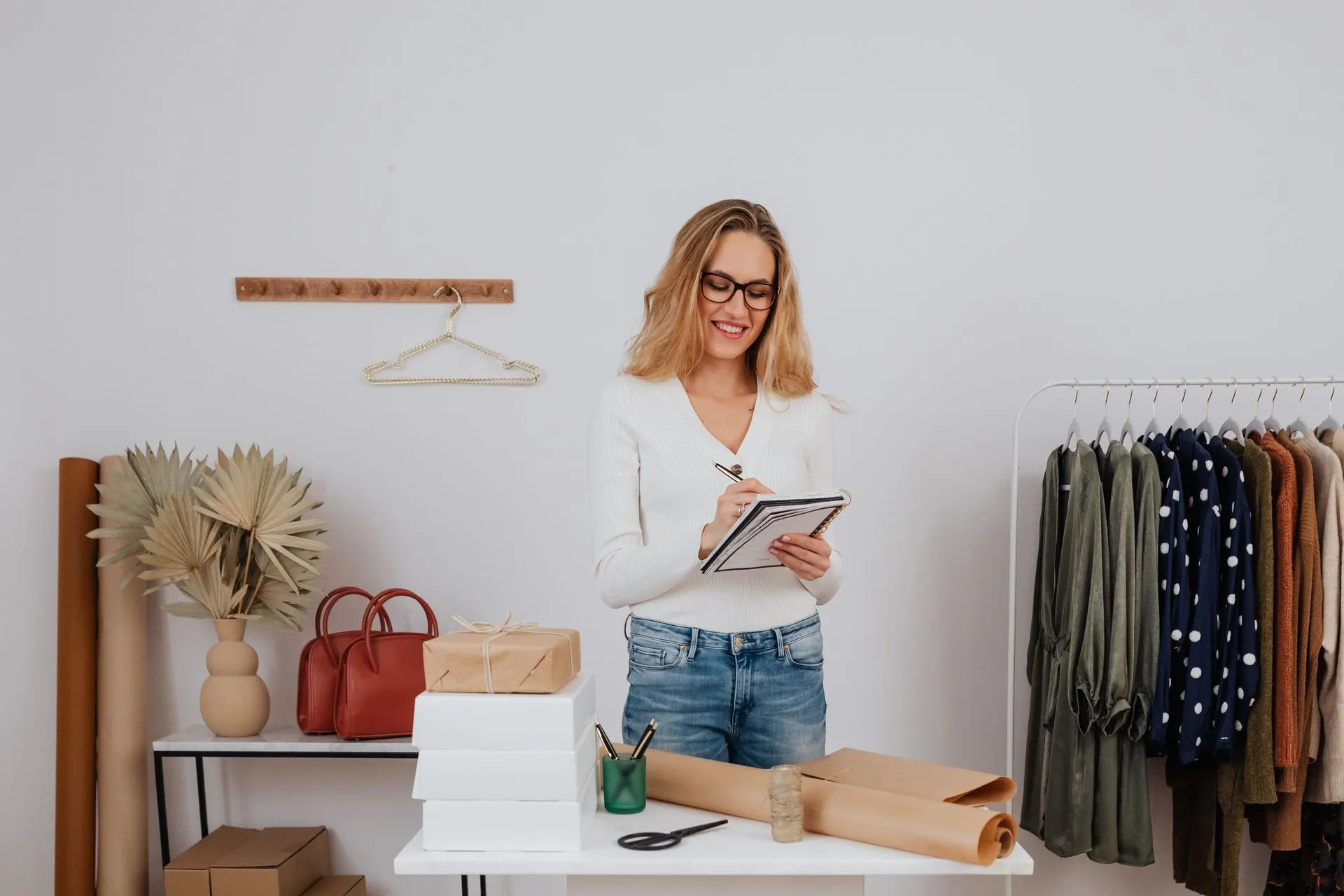 Boutique owner taking notes beside a clothing rack and wrapped gift boxes