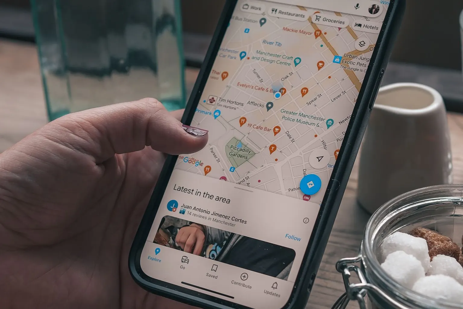 Hand holding a phone showing local businesses on Google Maps at a cafe table