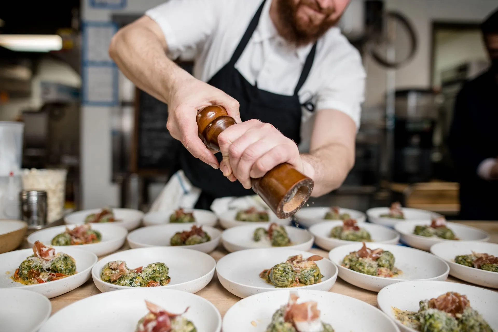 Cook seasoning a row of plated dishes in a busy restaurant kitchen