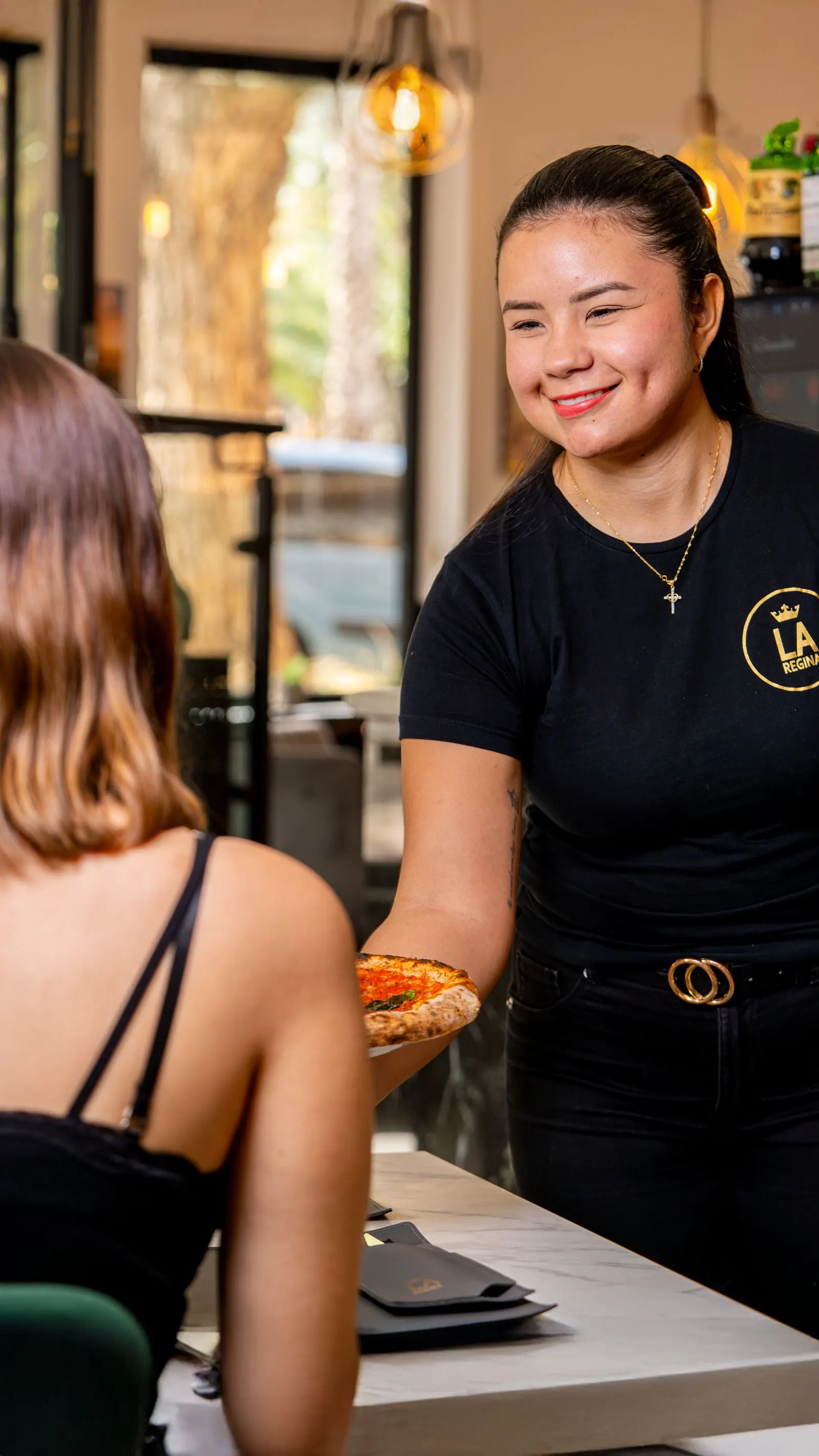 Server bringing a pizza to a customer's table at a casual restaurant